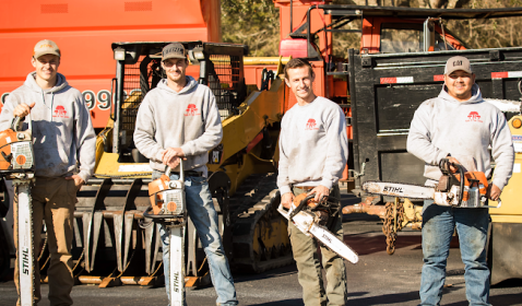 Four men from Triple R Tree Service standing in front of tree removing equipment. All of them are holding chainsaws.